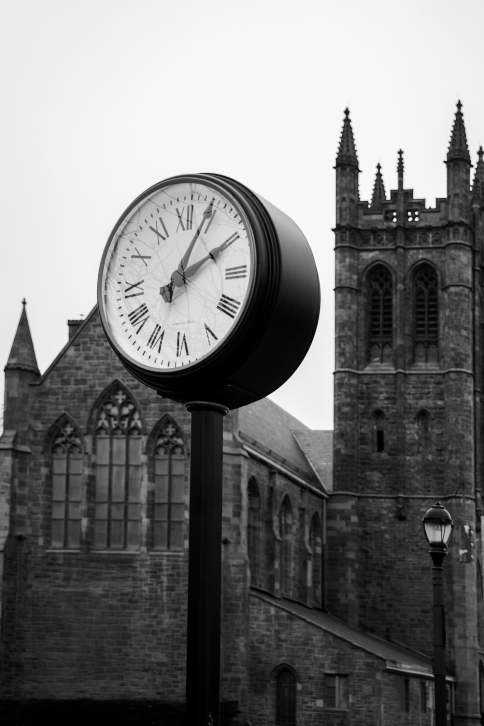 A street clock standing in front of a Gothic stone church